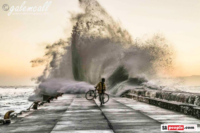 Cyclist with large wave at Kalk Bay Harbour