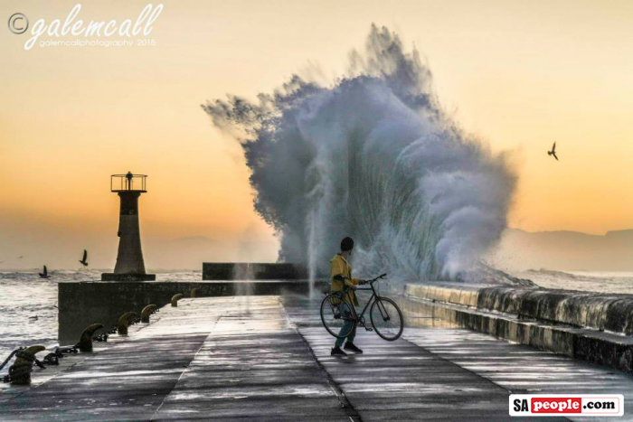 Cyclist with large wave at Kalk Bay Harbour