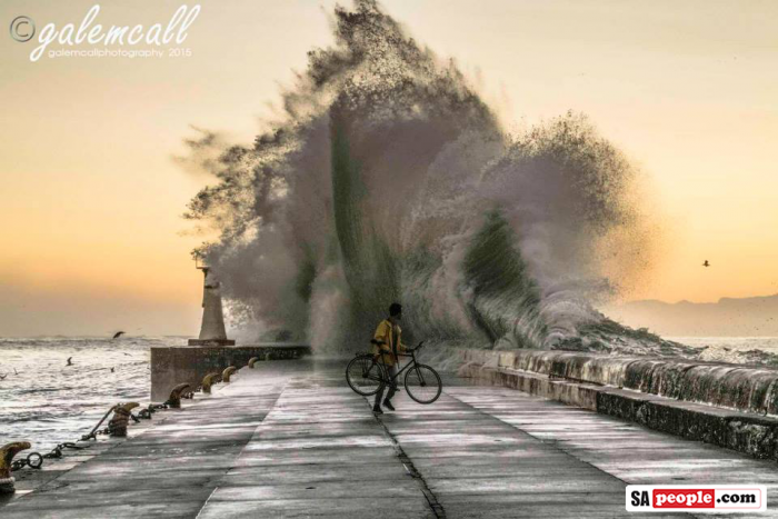 Cyclist with large wave at Kalk Bay Harbour