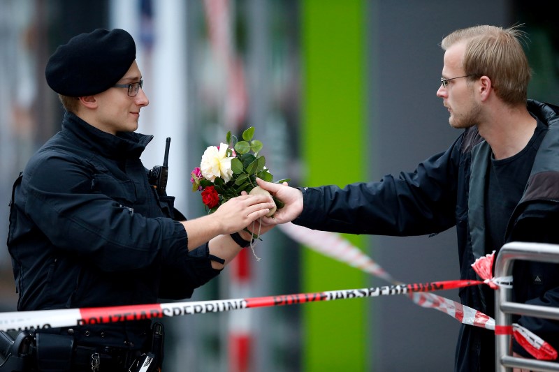A pedestrian hands flowers to a policeman to place it near the Olympia shopping mall, where yesterday's shooting rampage started, in Munich, Germany, July 23, 2016.   REUTERS/Michael Dalder
