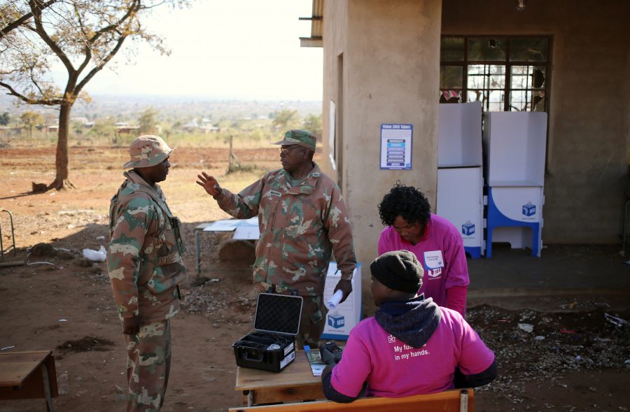 A member of the South African National defence Force (SANDF) gestures next to IEC officials as they set up preparing for voters at a school which was damaged during riots in May, now used as a polling station during tense local municipal elections in Vuwani, South Africa's northern Limpopo province, August 3, 2016. REUTERS/Siphiwe Sibeko