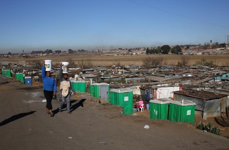 Women carry buckets with water on their heads as they make their way past a line of public toilets at a Kliptown informal settlement, Soweto. August 5,2016. REUTERS/Siphiwe Sibeko