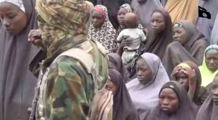 A still image from a video posted by Nigerian Islamist militant group Boko Haram on social media and seen by Reuters on August 14, 2016, shows a masked man talking to dozens of girls, one of them holding a baby, who the group said are school girls kidnapped in the town of Chibok in 2014. Social Media