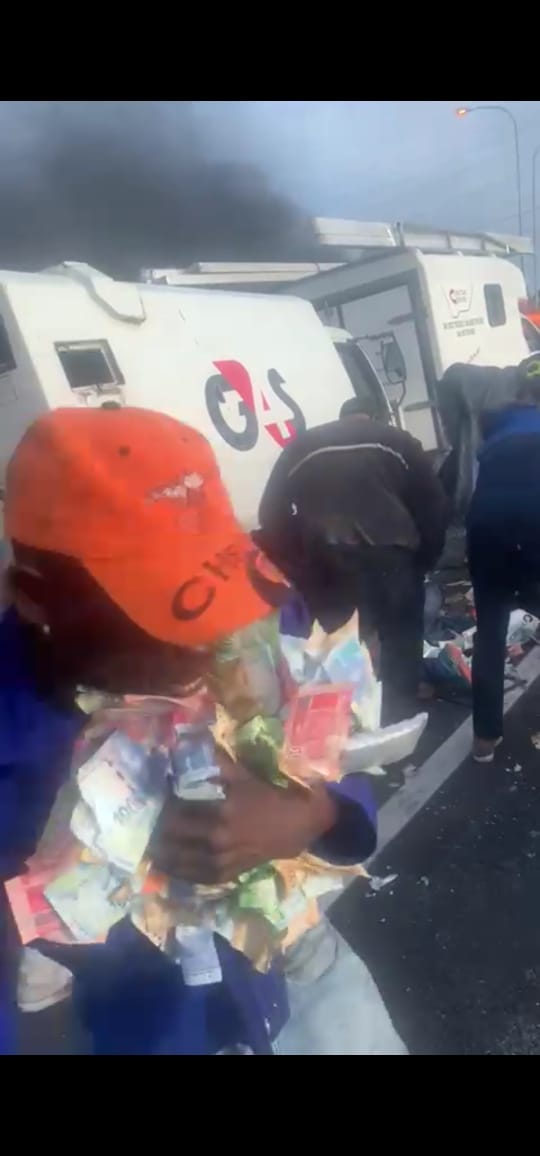 A looter with his arms full of looted cash clutching R10 (50p), R20 (£1), R50 (£2.50), R 100 (£5) and R200 (£10) notes scooped up from the motorway after robbers blew up an armoured cash track blowing money 100 feet up into the air