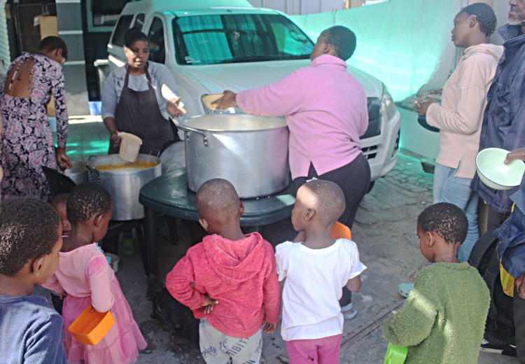Phathiswa Madyongolo and Noholide Ngcongca serve food to Pheliswa Ngubo at the soup kitchen in Mfuleni. Photos: Masixole Feni