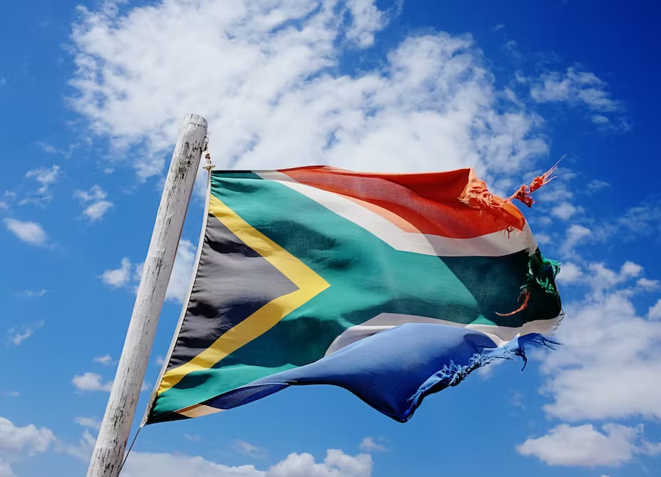 29 years of democracy has left its mark. Rather battered and frayed South African flag billowing in the wind against a cloud-strewn sky.