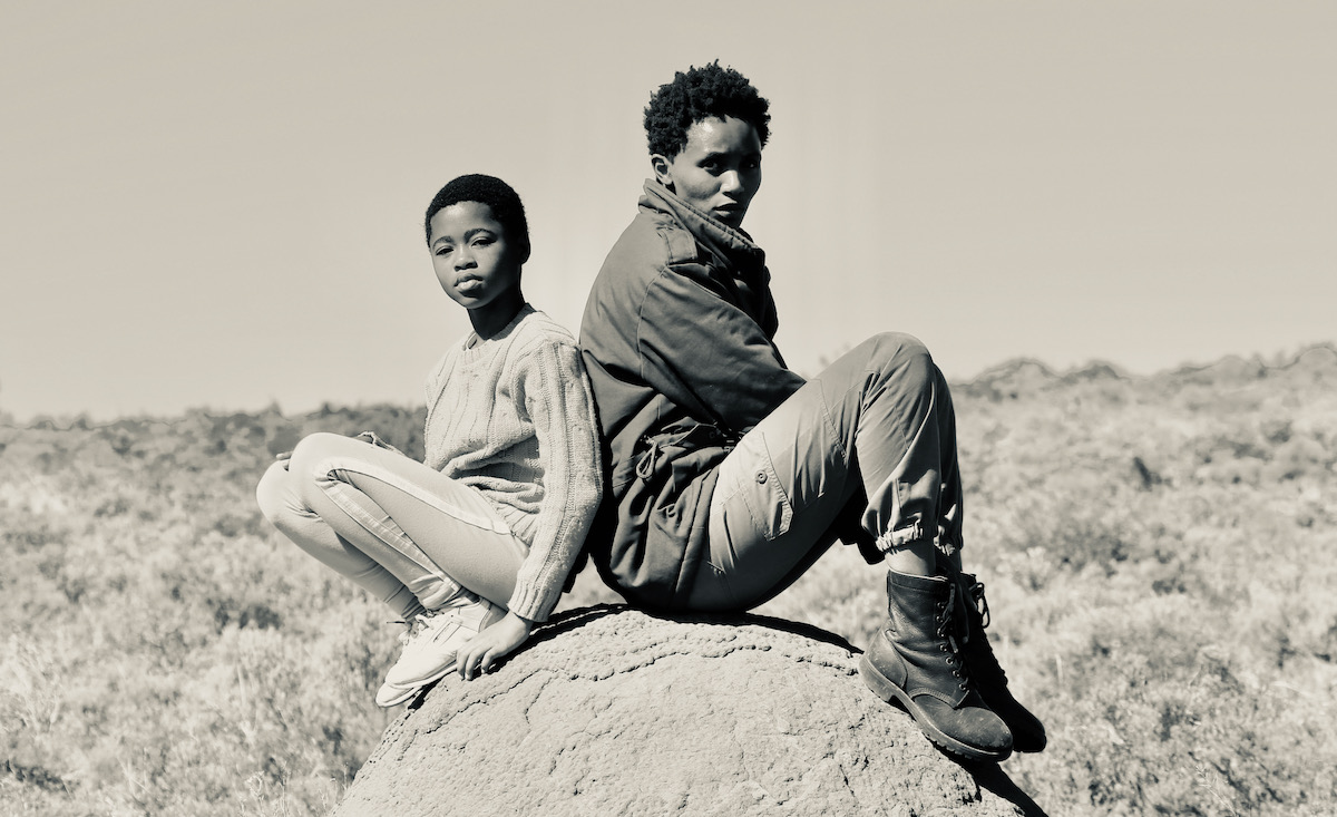 Liyabona Mroqoza and Avumile Qongqo sitting back to back, in sepia.