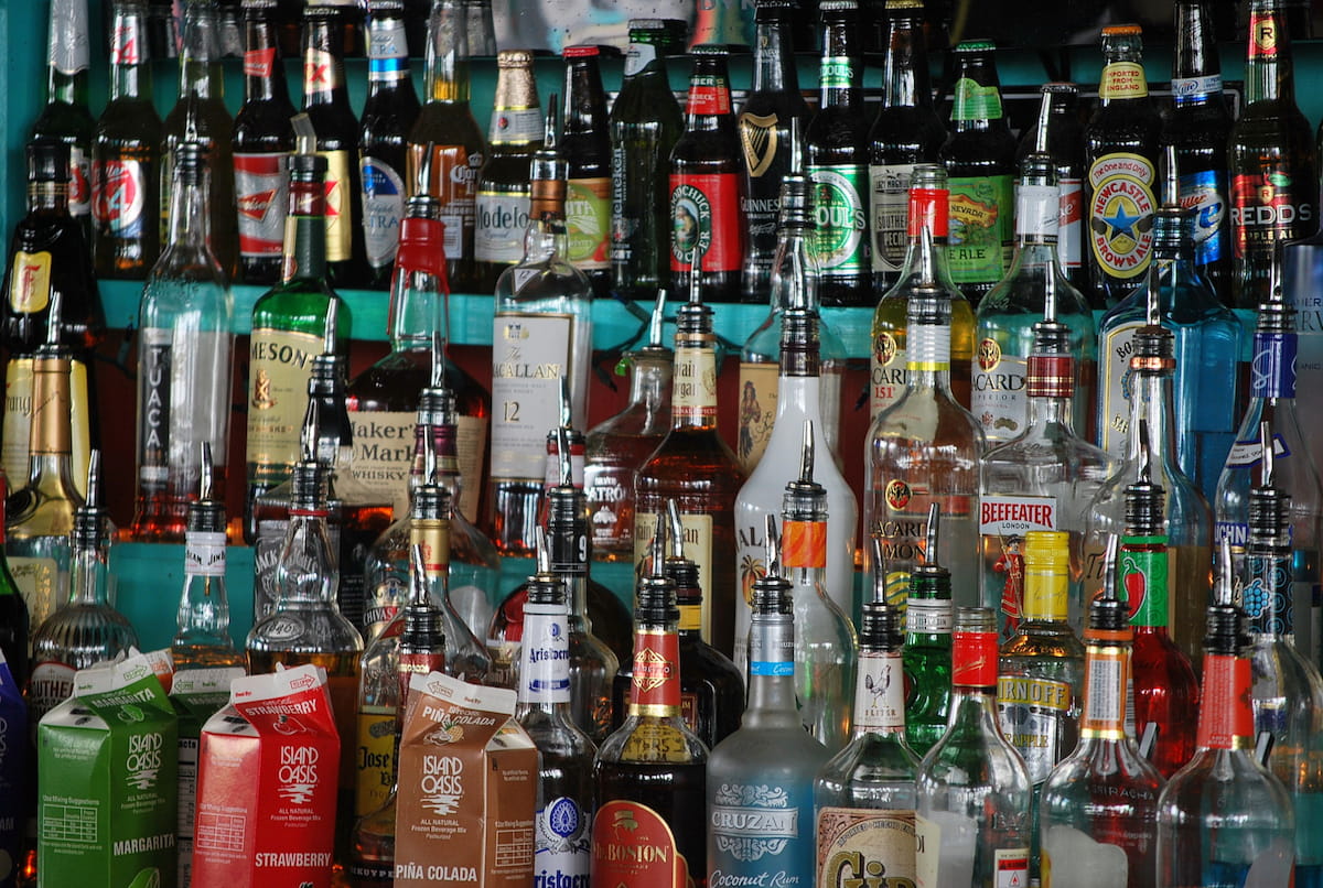 Image of assorted-color glass bottle lot at a bar. This image accompanies an article from the CPi about alcohol price in South Africa, shown by province