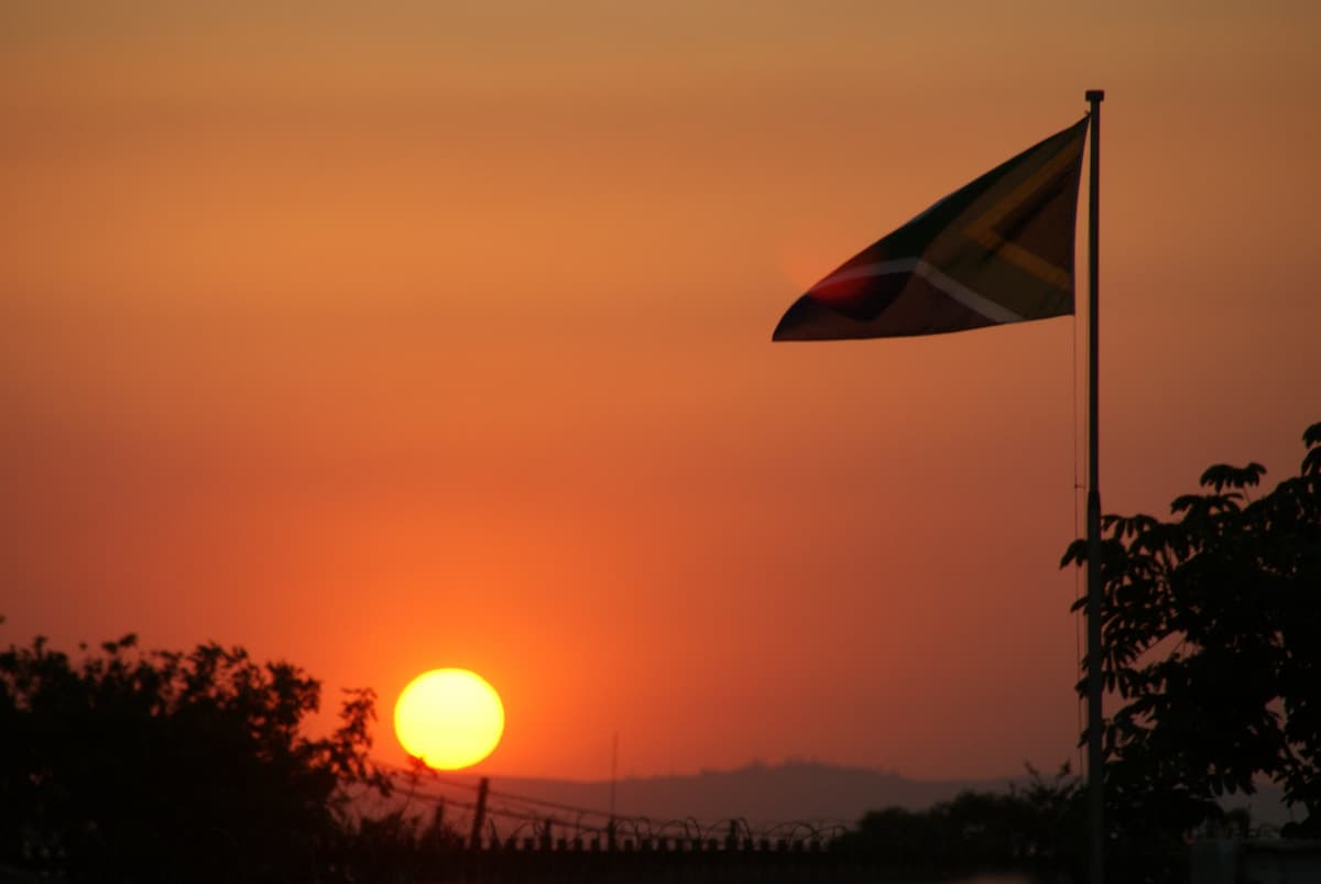 Image of the South African national flag in the sunset, accompanying an article about South Africa's elderly population boom and implications for Old Age Grant, as forecast by Stats SA